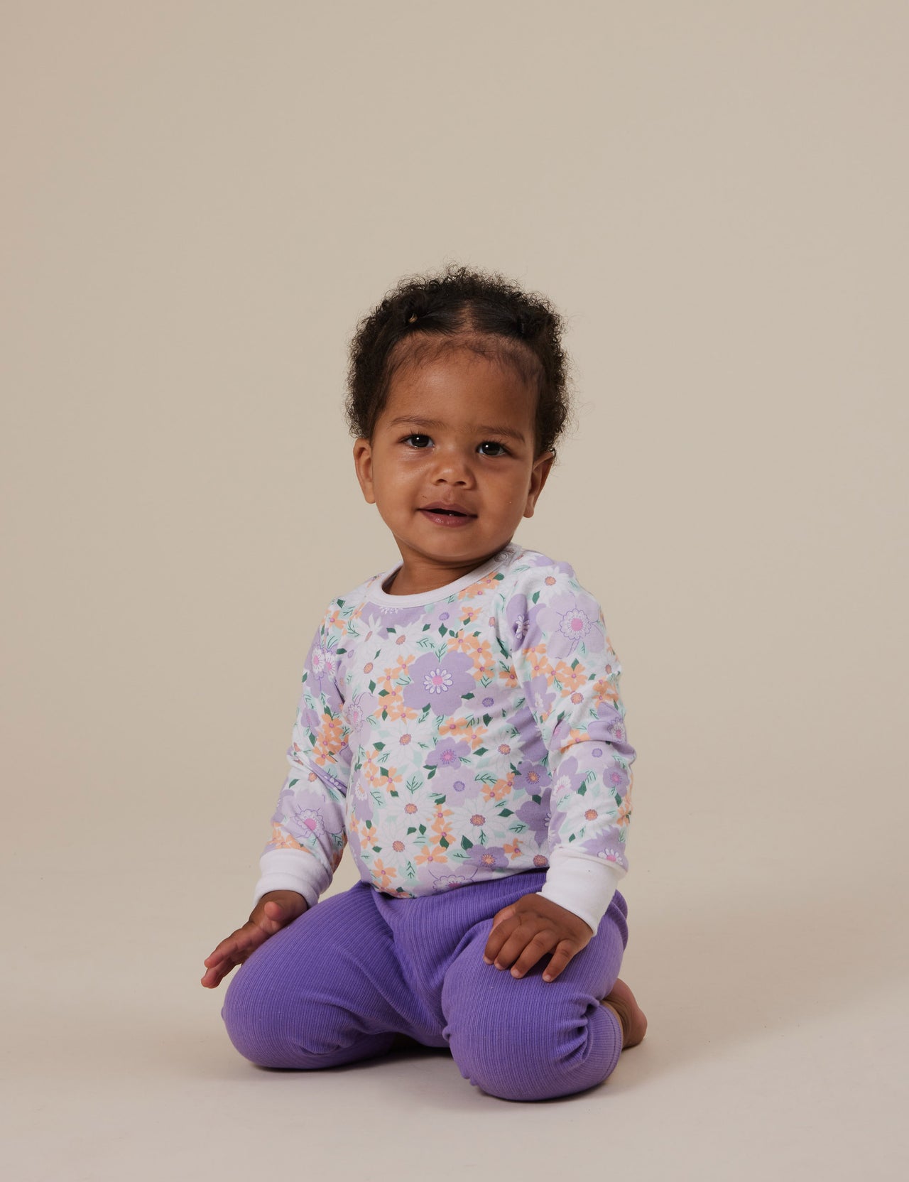 The Goldie + Ace Flora Long Sleeve Bodysuit in Lilac Multi pictured on a grey background. The material is soft cotton elastane. It is a babywear made for babies, toddlers and kids.
