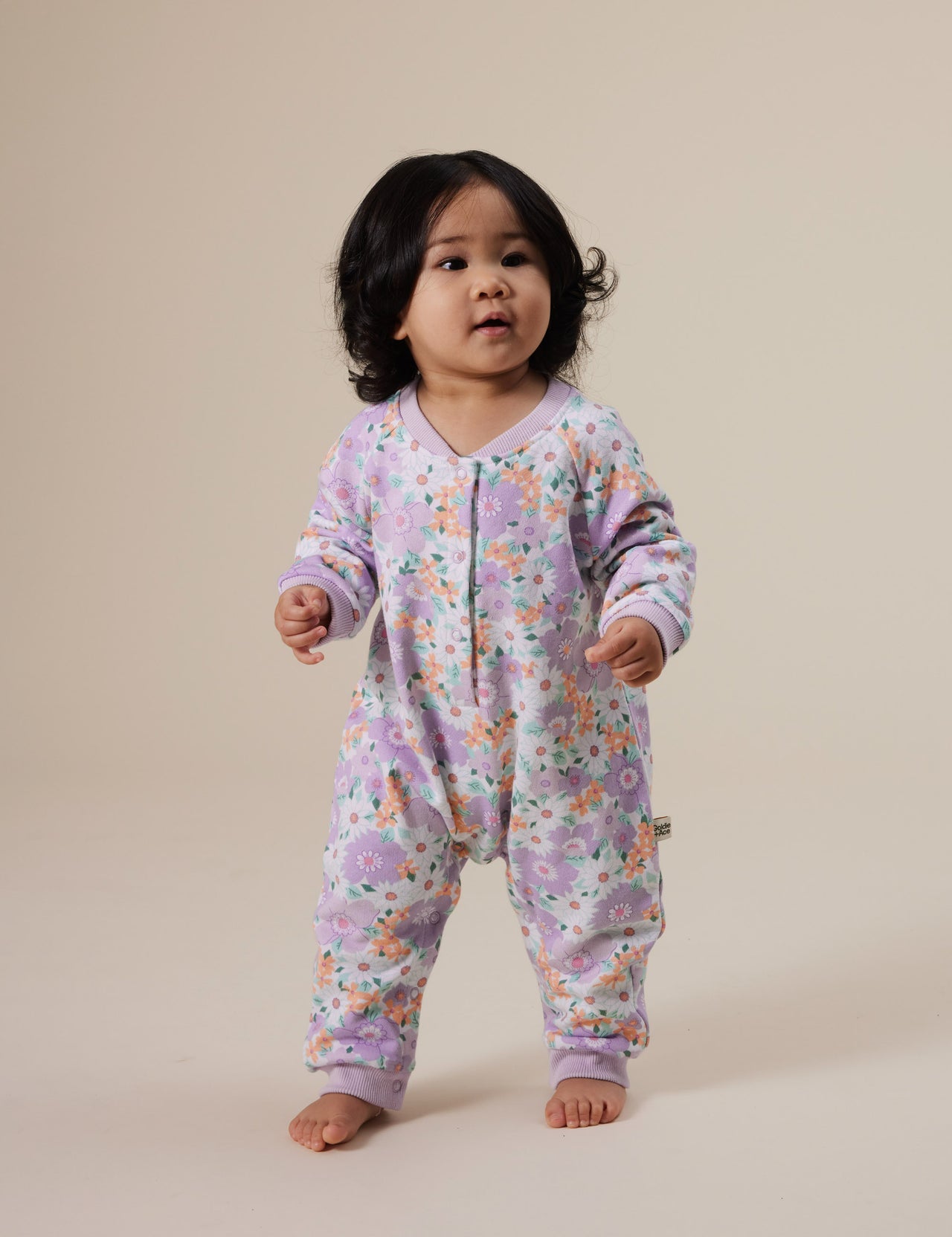 The Goldie + Ace Flora Relaxed Terry Romper in Lilac Multi pictured on a grey background. The material is cotton terry. It is a babywear made for babies, toddlers and kids.