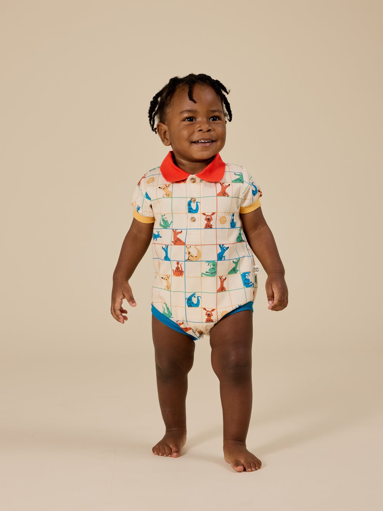 The Goldie + Ace Hopscotch Polo Romper in Vanilla/Primary pictured on a transparent background. The material is 100% cotton. It is a romper made for babies, toddlers and kids.