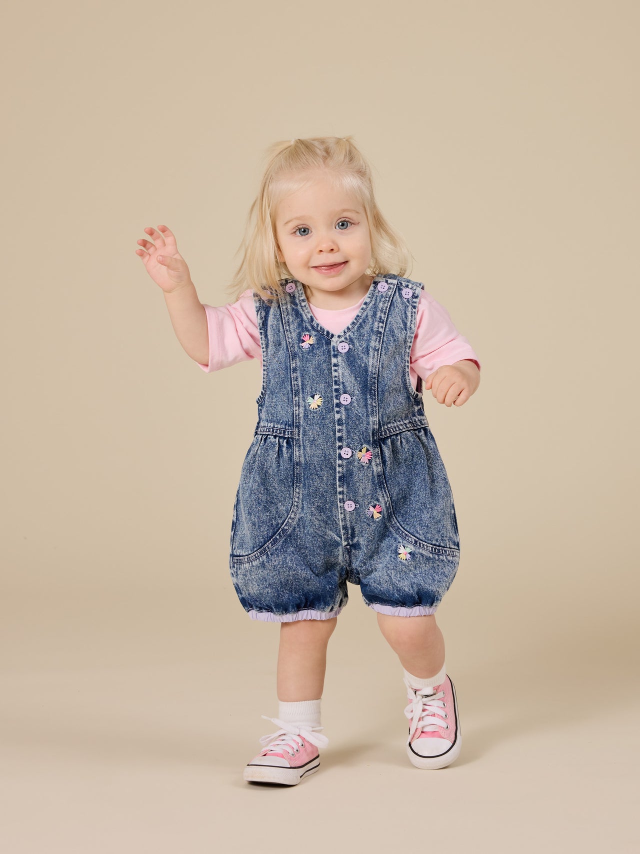 The Goldie + Ace Nina Pastel Petals Denim Romper in Dark Denim pictured on a transparent background. The material is 100% cotton. It is a romper made for babies, toddlers and kids.
