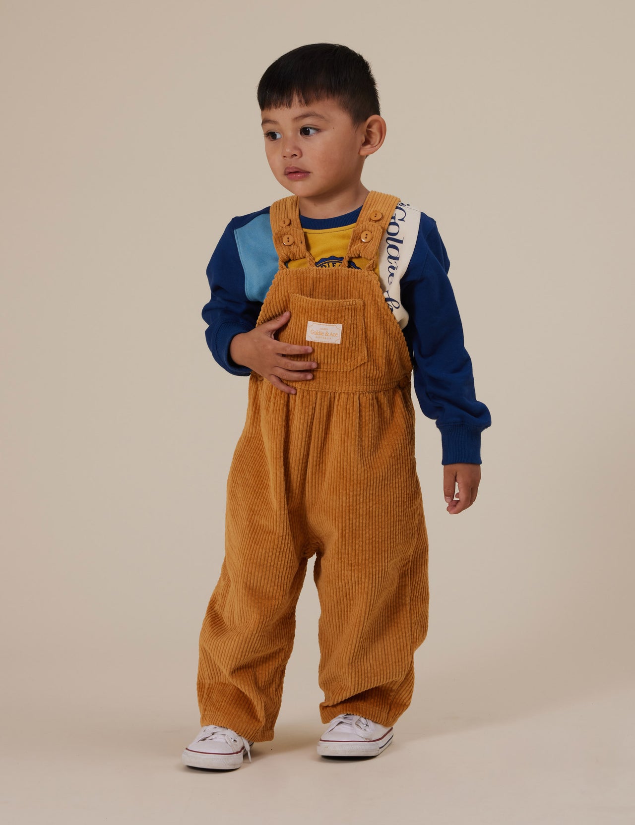 The Goldie + Ace Sammy Corduroy Overalls in Golden pictured on a grey background. The material is cotton cord. It is a overall made for babies, toddlers and kids.