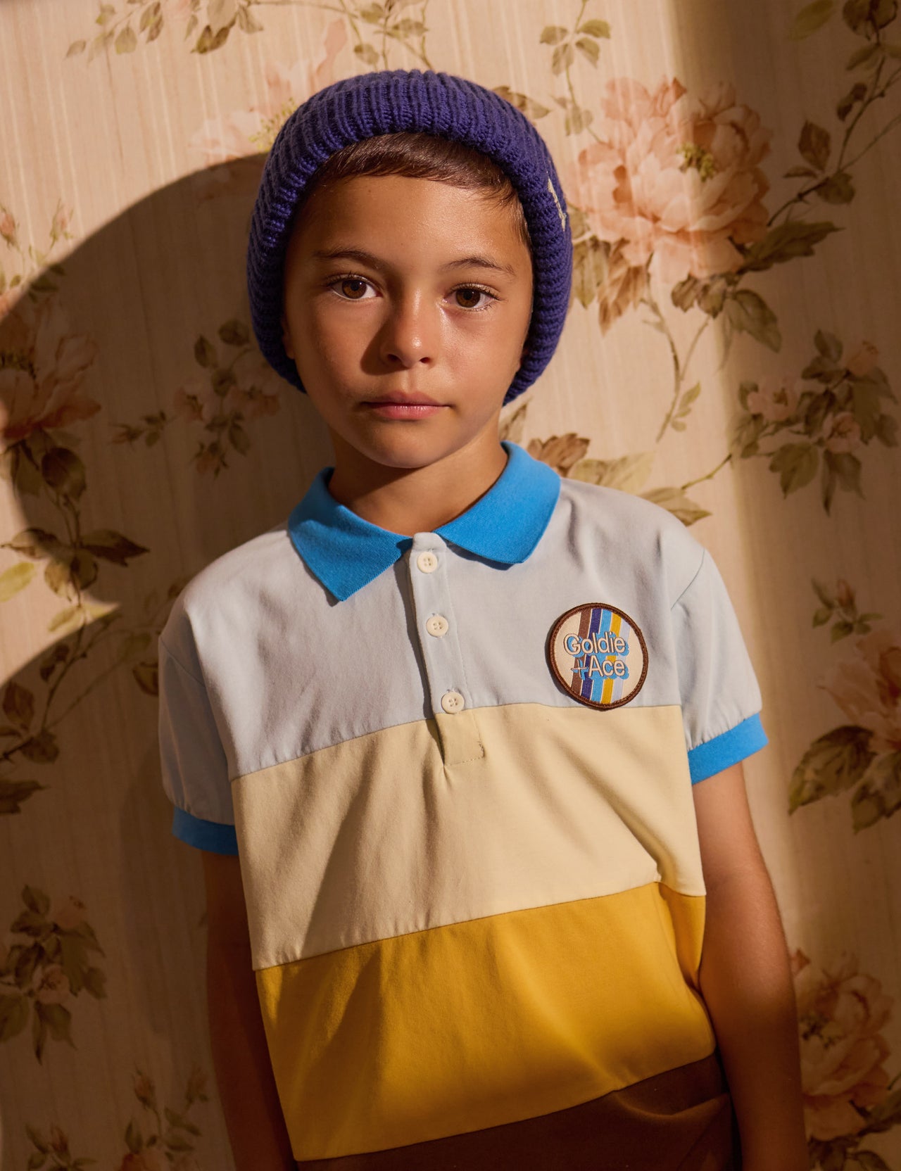 The Goldie + Ace Tommy Polo Shirt in Brown Golden Cream Blue pictured on a grey background. The material is cotton jersey. It is a top made for babies, toddlers and kids.
