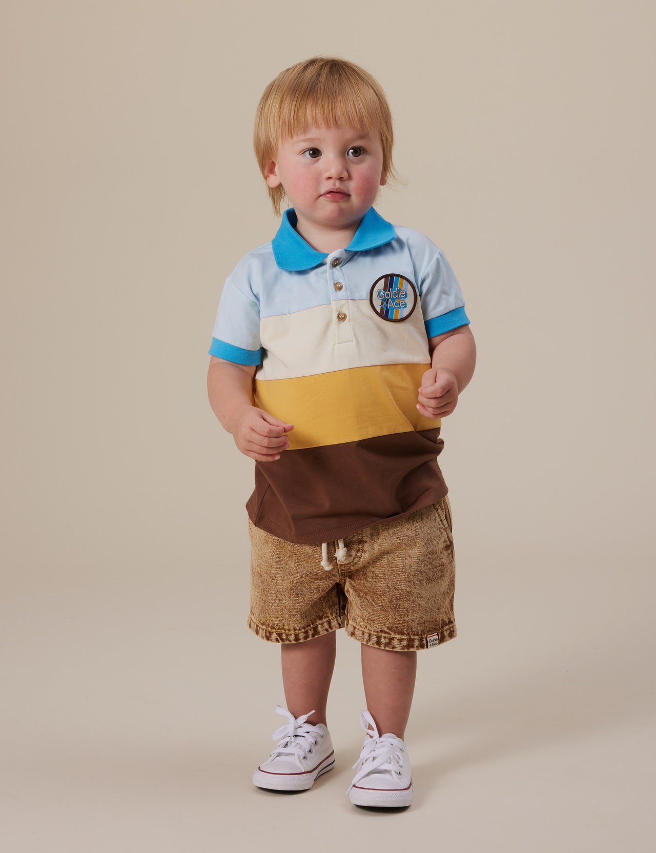The Goldie + Ace Tommy Polo Shirt in Brown Golden Cream Blue pictured on a grey background. The material is cotton jersey. It is a top made for babies, toddlers and kids.
