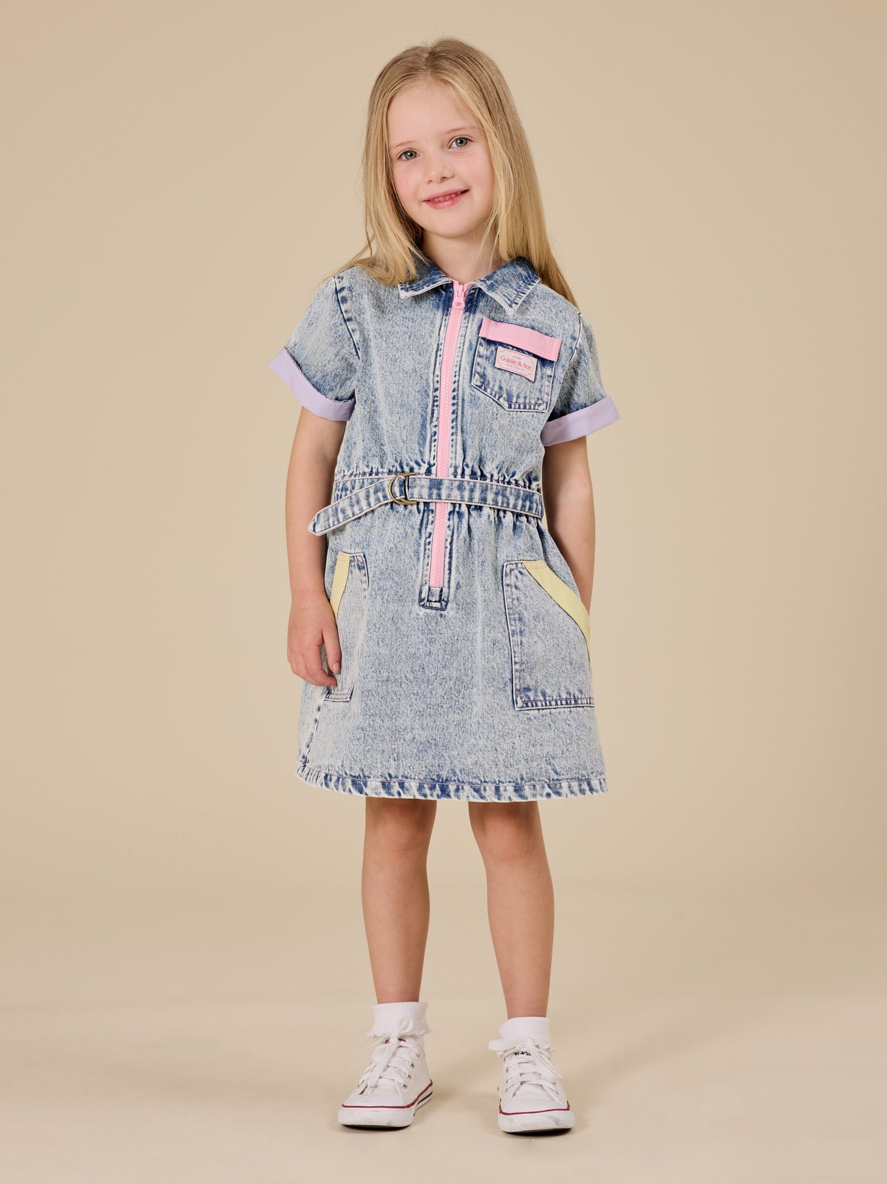 The Goldie + Ace Pastel Pop Piper Denim Belted Dress in Light Denim pictured on a transparent background. The material is cotton. It is a dress made for babies, toddlers and kids.