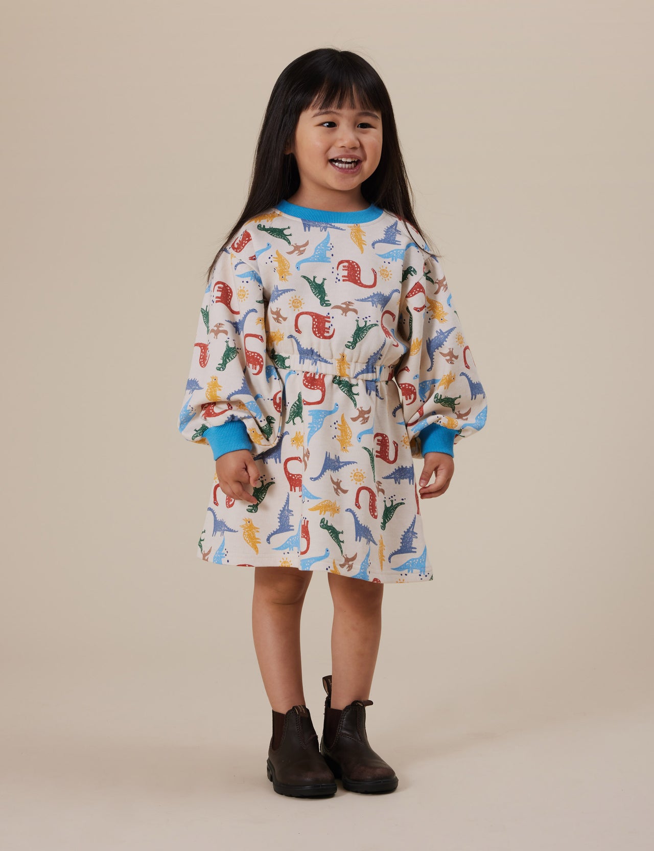 The Goldie + Ace Dino-Mite Leah Long Sleeve Dress in Multi pictured on a grey background. The material is cotton terry. It is a dress made for babies, toddlers and kids.