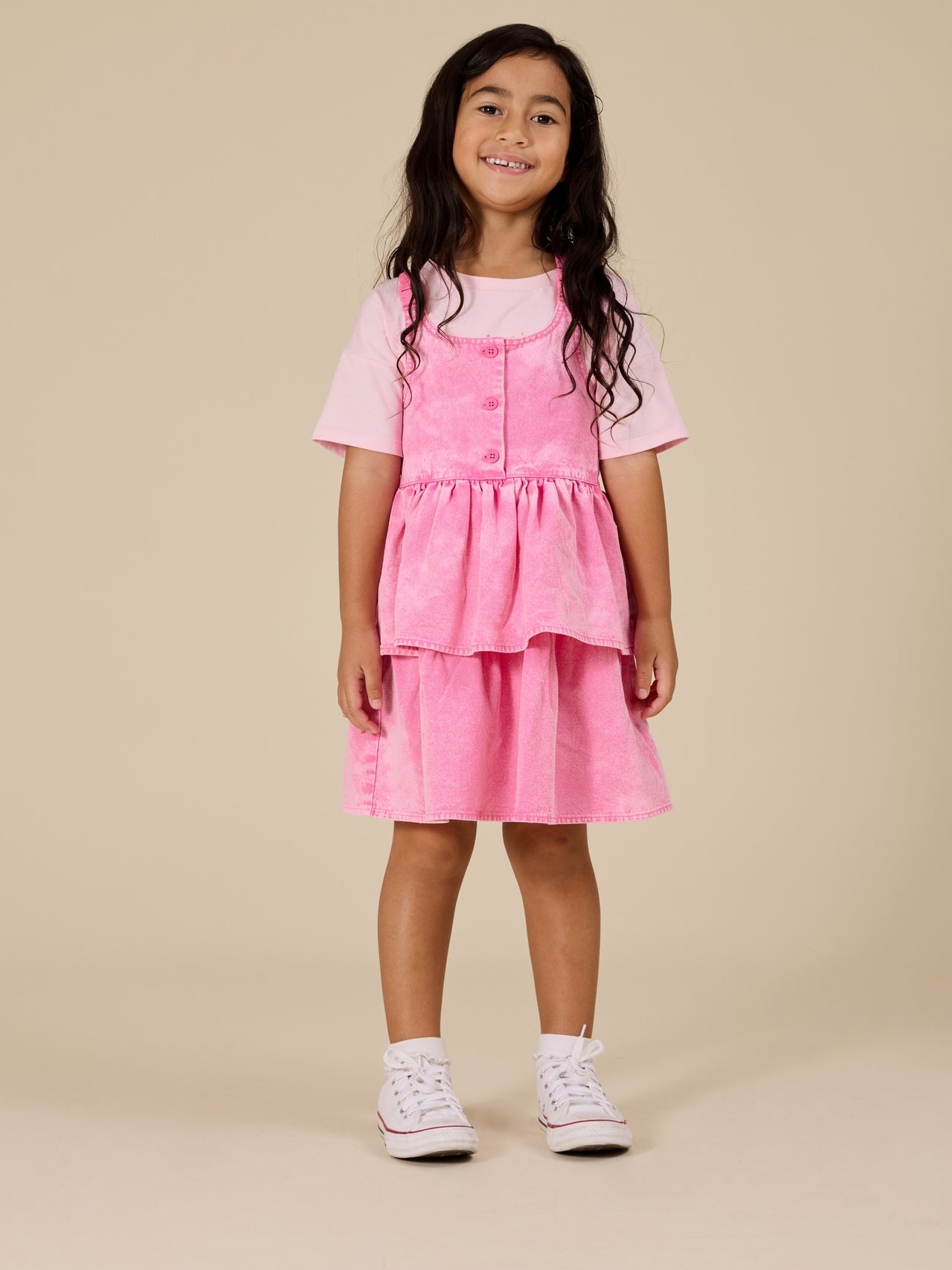The Goldie + Ace Saskia Denim Frill Pinafore Dress in Pink Lemonade pictured on a transparent background. The material is cotton. It is a dress made for babies, toddlers and kids.
