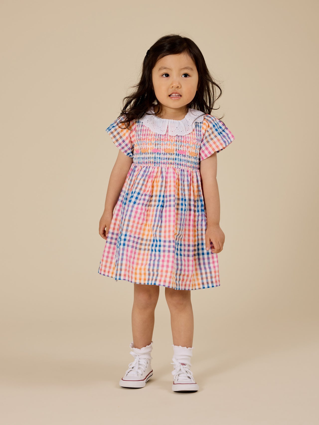 The Goldie + Ace Rainbow Gingham Flo Smocked Dress in Multi pictured on a transparent background. The material is cotton with cotton lining. It is a dress made for babies, toddlers and kids.