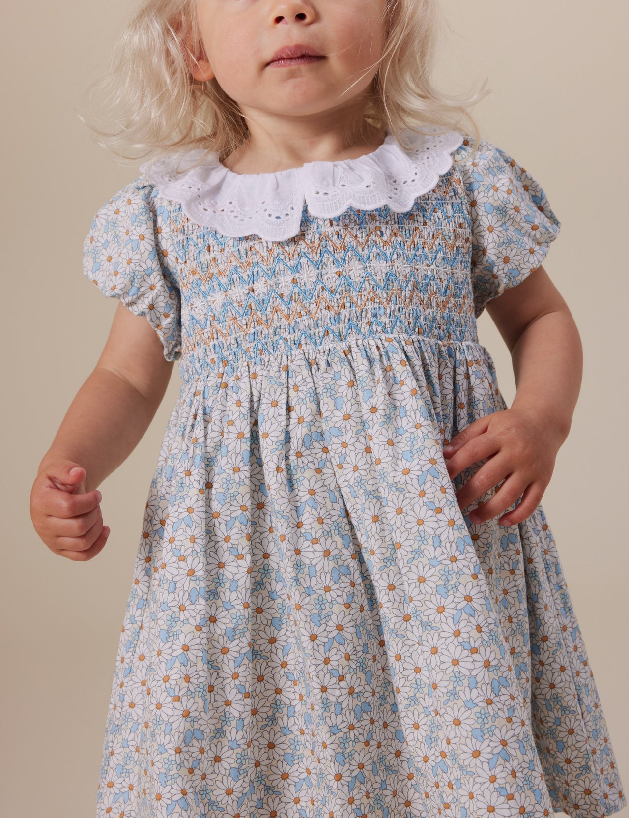 The Goldie + Ace Sunny Floral Flo Smocked Dress in Sunny Floral pictured on a grey background. The material is cotton. It is a dress made for babies, toddlers and kids.