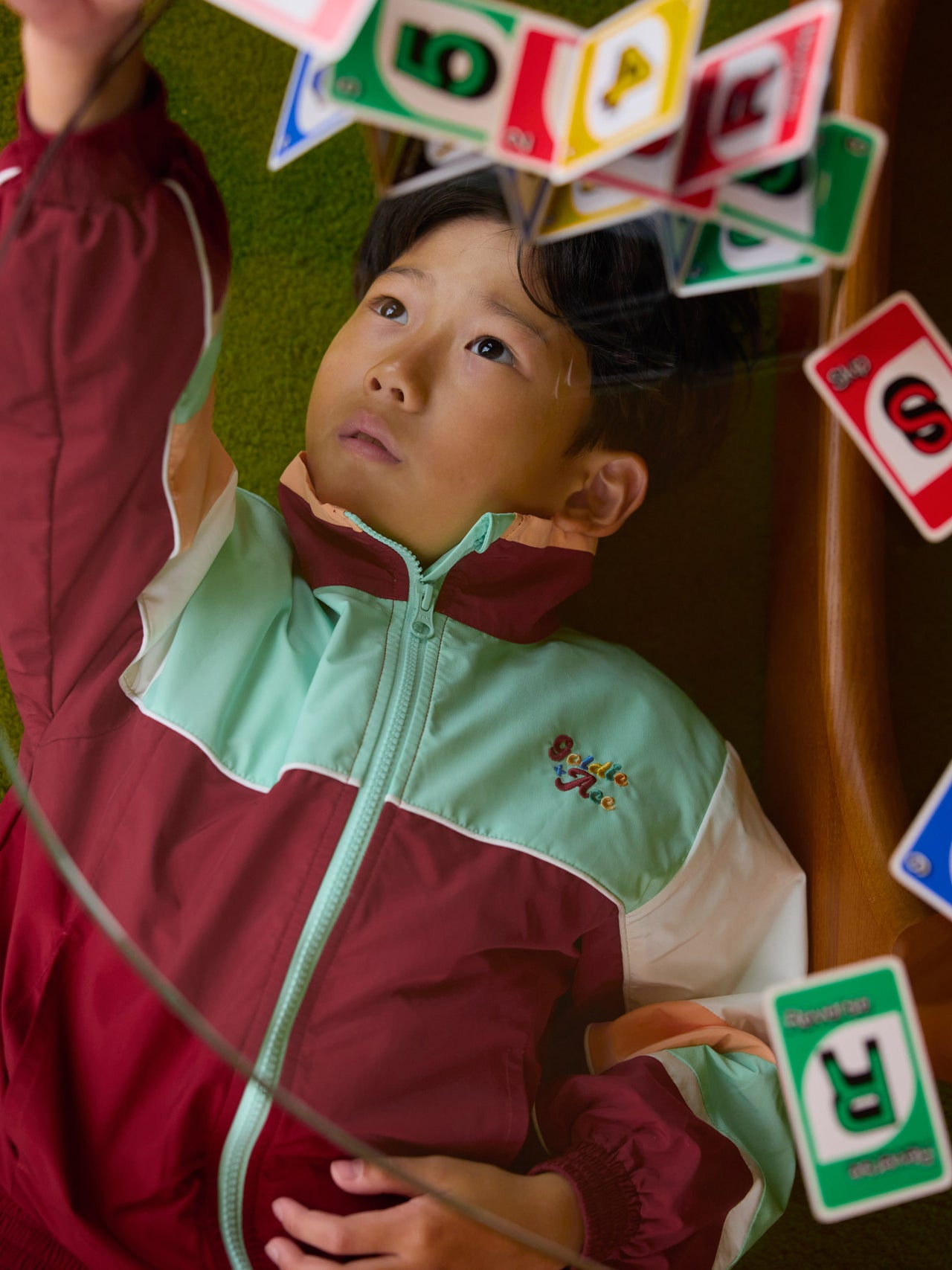 The Goldie + Ace Fun Run Retro Spray Jacket in Brick/Peapod pictured on a transparent background. The material is poly with cotton lining. It is a jacket made for babies, toddlers and kids.