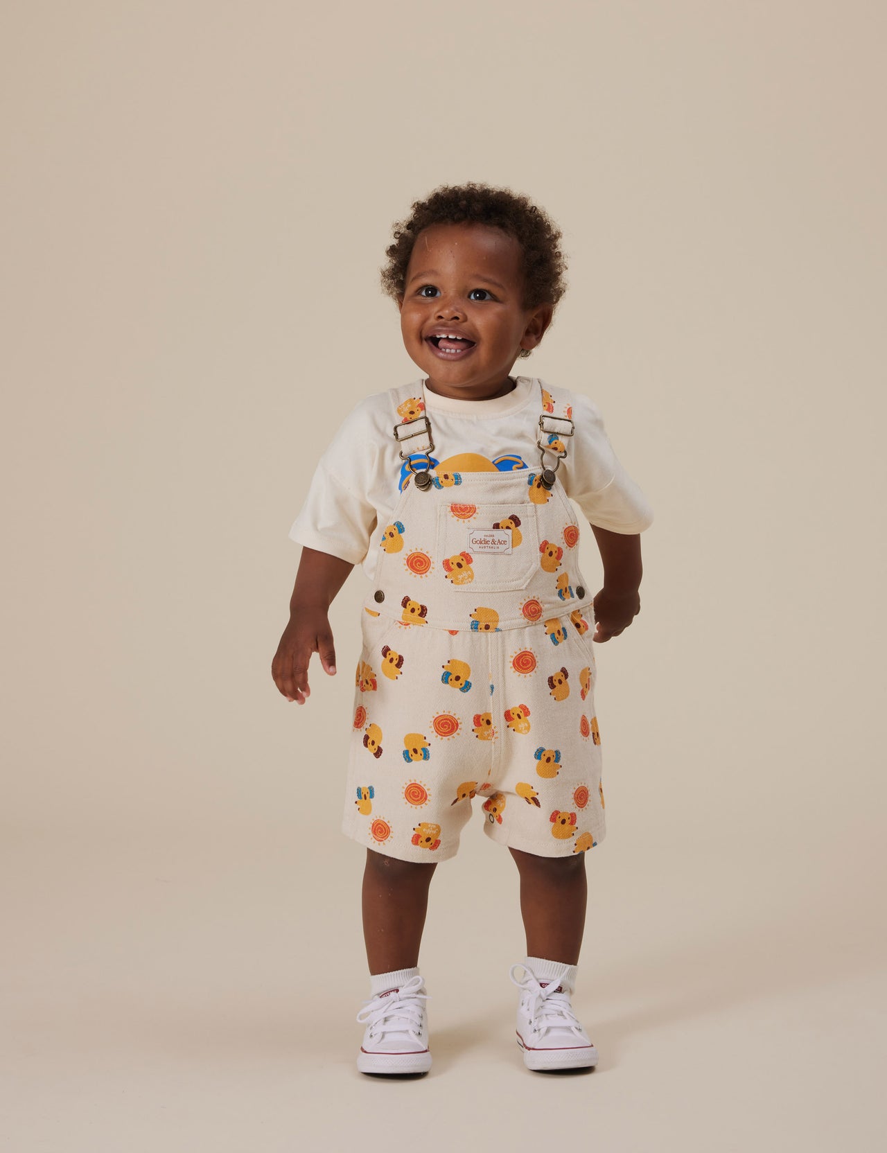 The Goldie + Ace Koala Puff Print T-Shirt in Ivory pictured on a grey background. The material is cotton jersey. It is a top made for babies, toddlers and kids.