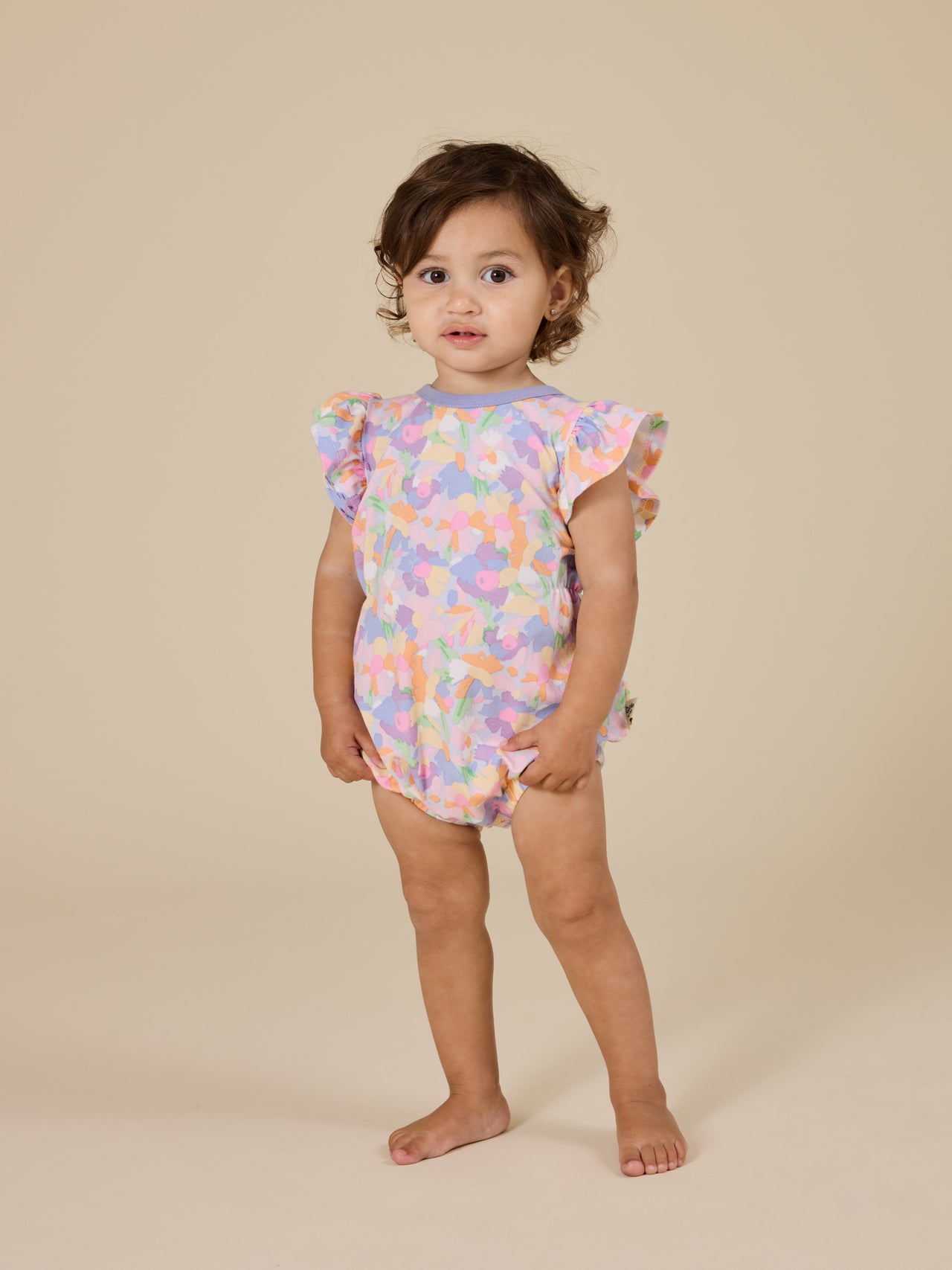 The Goldie + Ace Pastel Bouquet Frill Bubble Romper in Lilac Multi pictured on a transparent background. The material is soft cotton elastane. It is a romper made for babies, toddlers and kids.