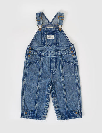 The Goldie + Ace Blake Vintage Washed Denim Overalls in Dark Denim pictured on a grey background. The material is cotton denim. It is a overall made for babies, toddlers and kids.