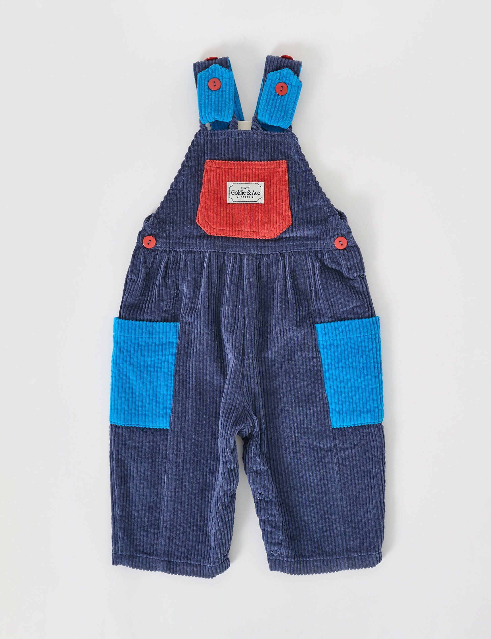 The Goldie + Ace Sammy Corduroy Colour Block Overalls in Blue/Red pictured on a grey background. The material is cotton denim. It is a overall made for babies, toddlers and kids.