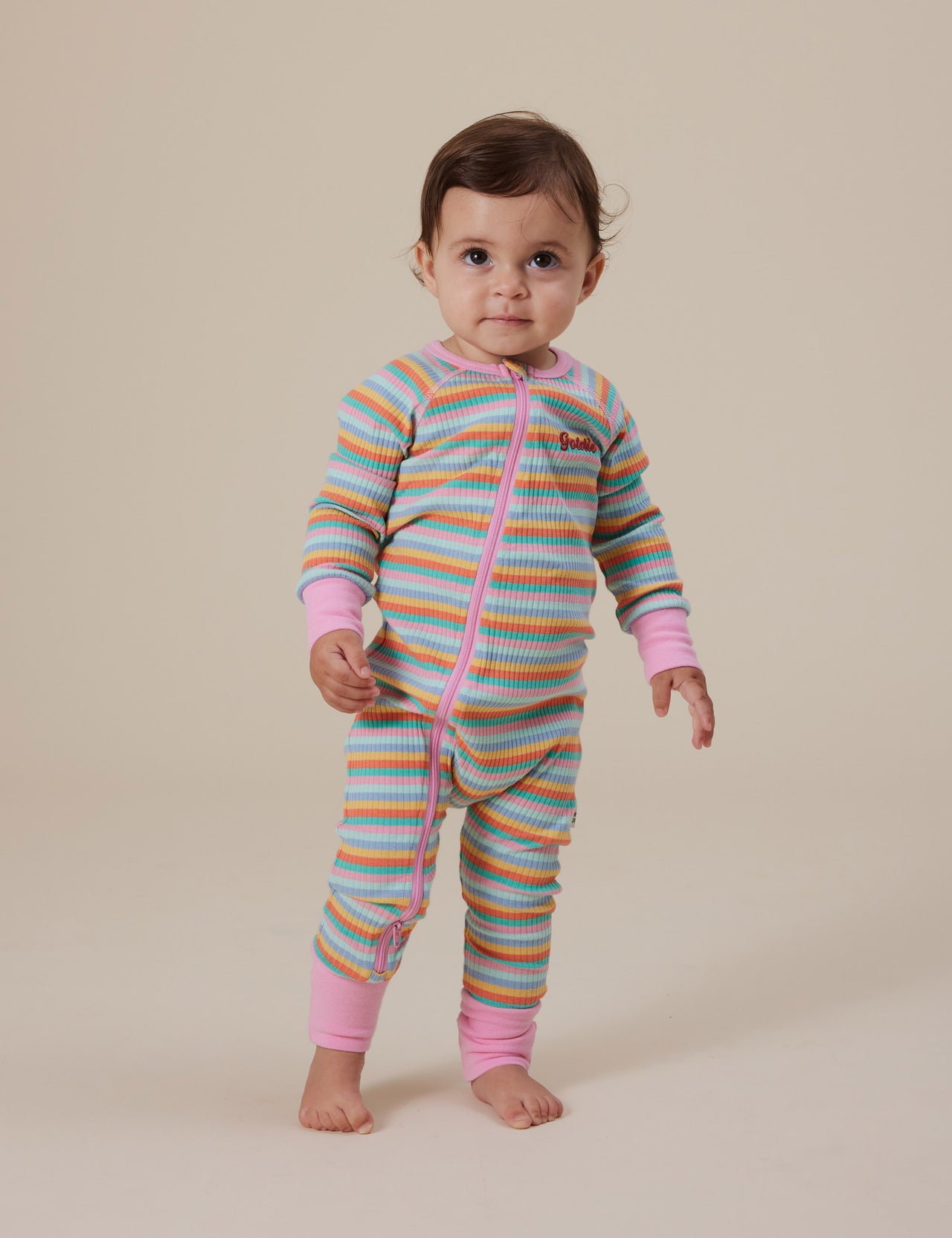 The Goldie + Ace Rib Zipsuit in Candy Stripe pictured on a grey background. The material is soft ribbed cotton elastane. It is a babywear made for babies, toddlers and kids.