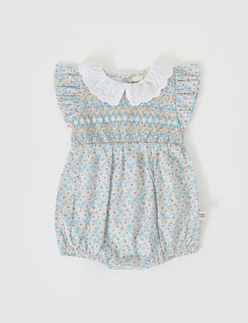 The Goldie + Ace Sunny Floral Lani Smocked Romper in Sunny Floral pictured on a grey background. The material is cotton. It is a babywear made for babies, toddlers and kids.