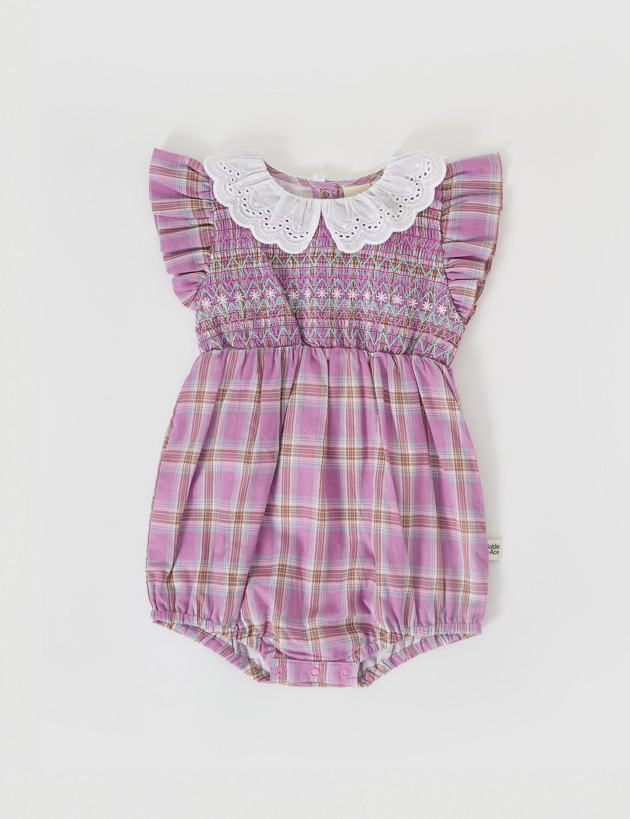 The Goldie + Ace Mauve Check Lani Smocked Romper in Mauve Check pictured on a grey background. The material is cotton. It is a babywear made for babies, toddlers and kids.