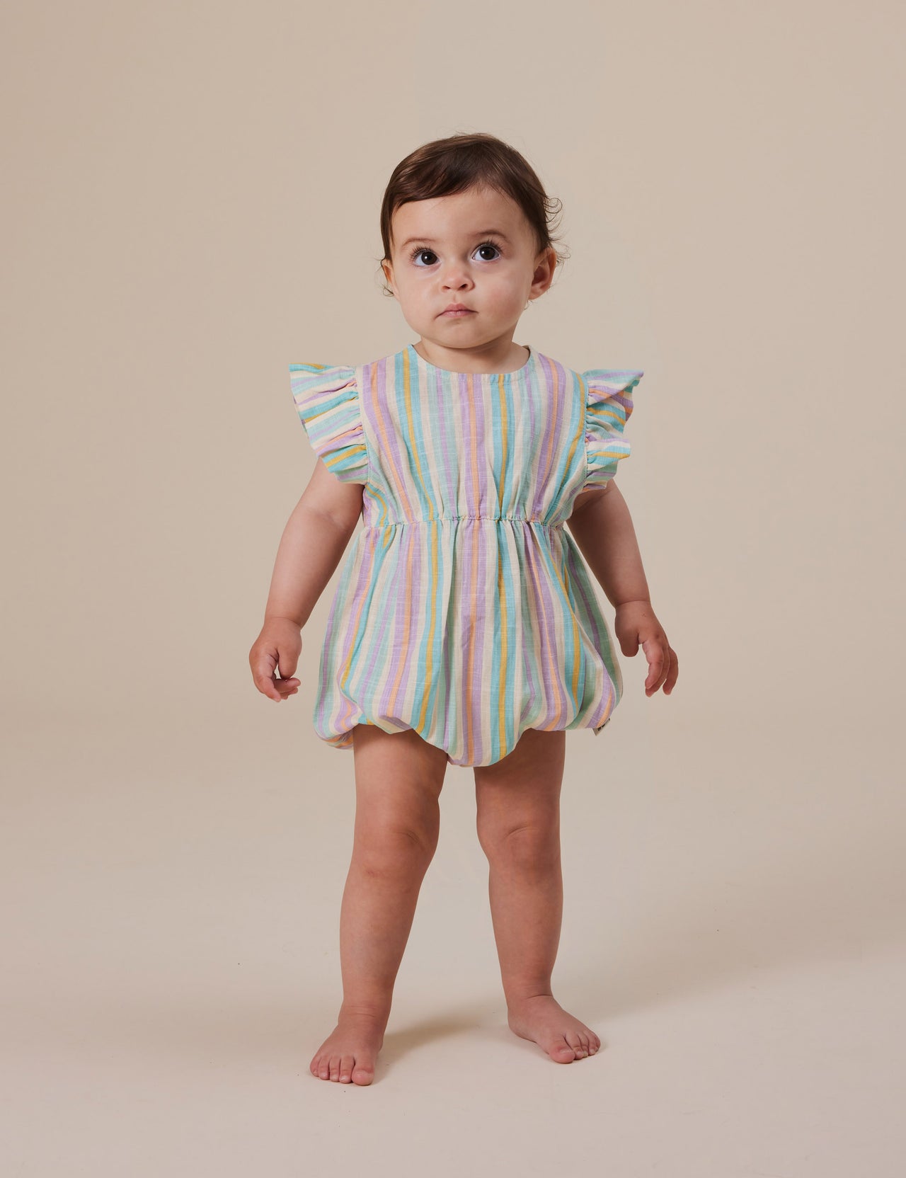 The Goldie + Ace Lani Linen Romper in Resort Stripe pictured on a grey background. The material is linen. It is a babywear made for babies, toddlers and kids.