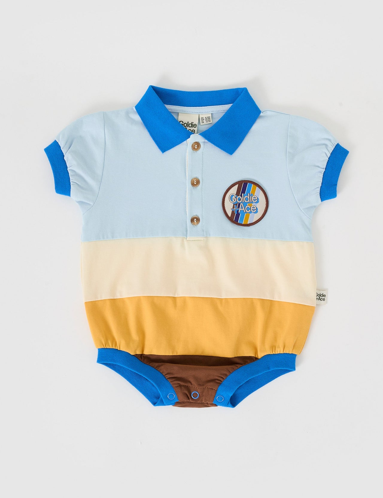 The Goldie + Ace Luca Polo Romper in Blue/Golden/Brown pictured on a grey background. The material is cotton jersey. It is a romper made for babies, toddlers and kids.