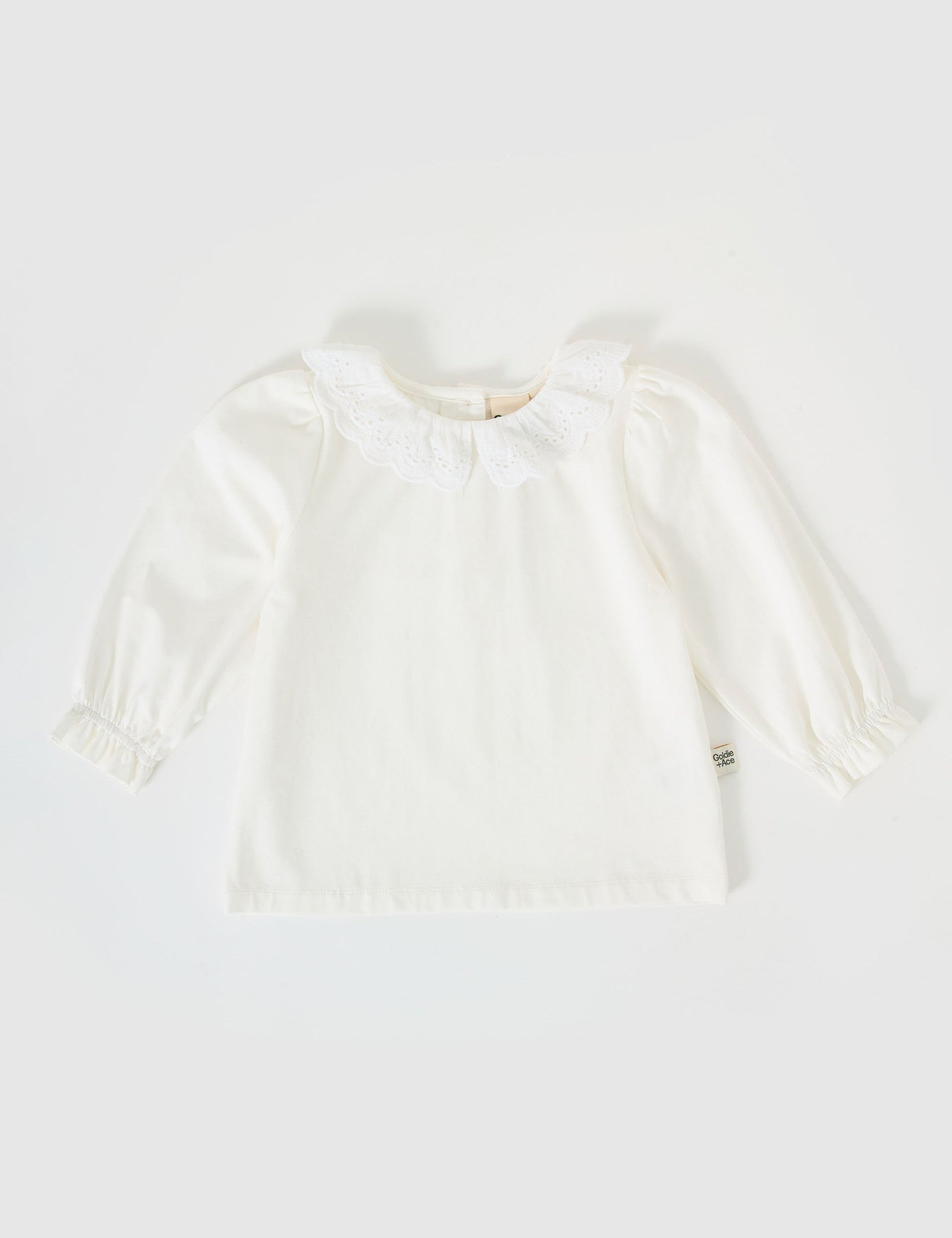 The Goldie + Ace Laura Puff Sleeve Collar Long Sleeve in White pictured on a grey background. The material is cotton jersey. It is a top made for babies, toddlers and kids.