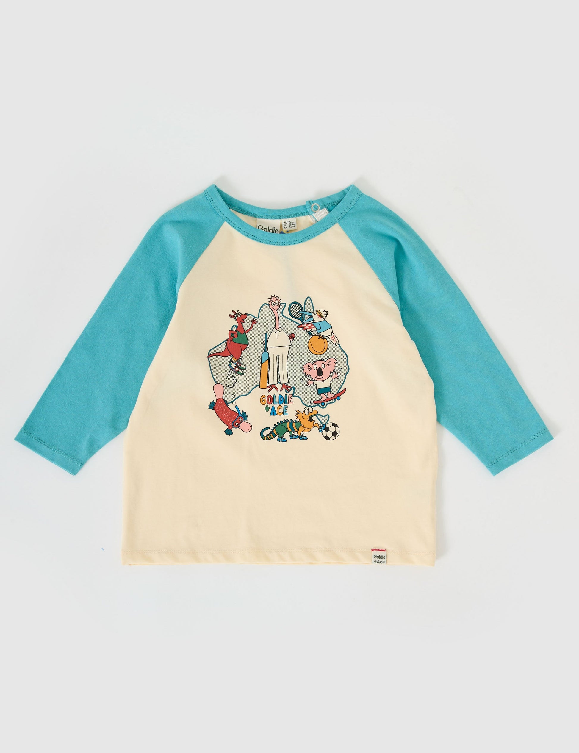 The Goldie + Ace Team Goldie Raglan Long Sleeve Top in Vanilla/Dusty Blue pictured on a grey background. The material is cotton jersey. It is a top made for babies, toddlers and kids.