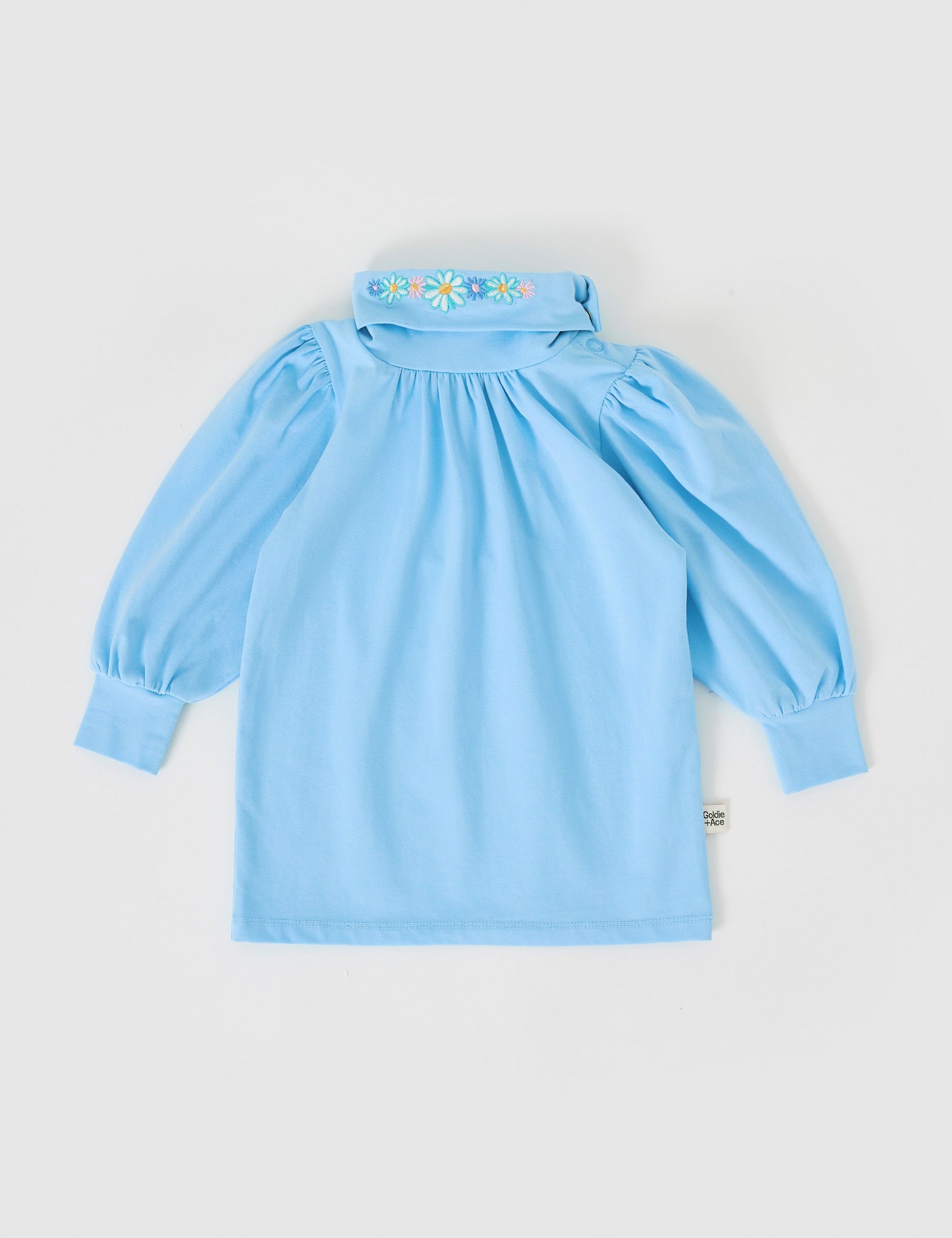 The Goldie + Ace Sofia Embroidered Puff Sleeve Skivvy in Sky Blue pictured on a grey background. The material is cotton jersey. It is a top made for babies, toddlers and kids.