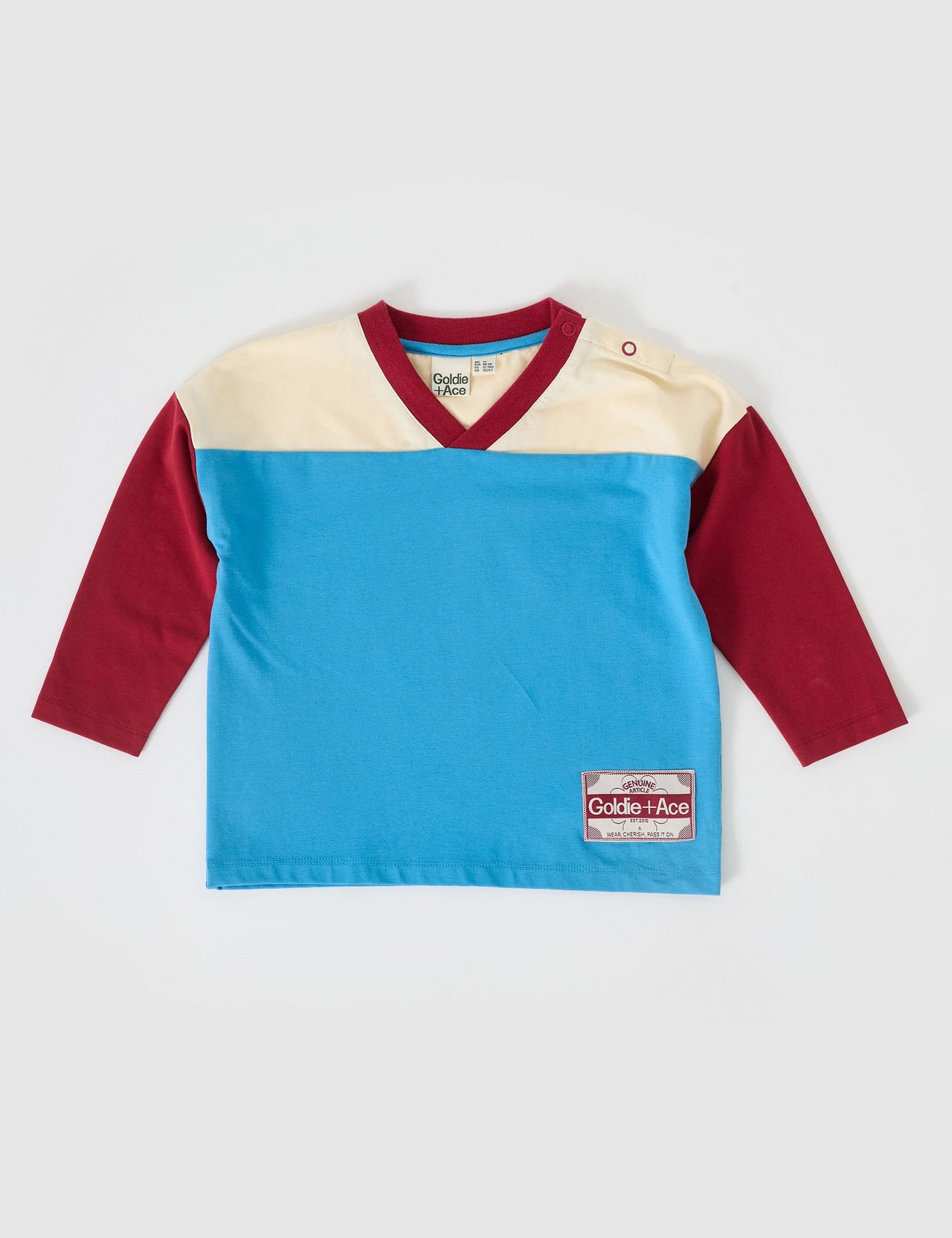 The Goldie + Ace Chip Long Sleeve Jersey in Blue/Burgundy pictured on a grey background. The material is cotton jersey. It is a top made for babies, toddlers and kids.