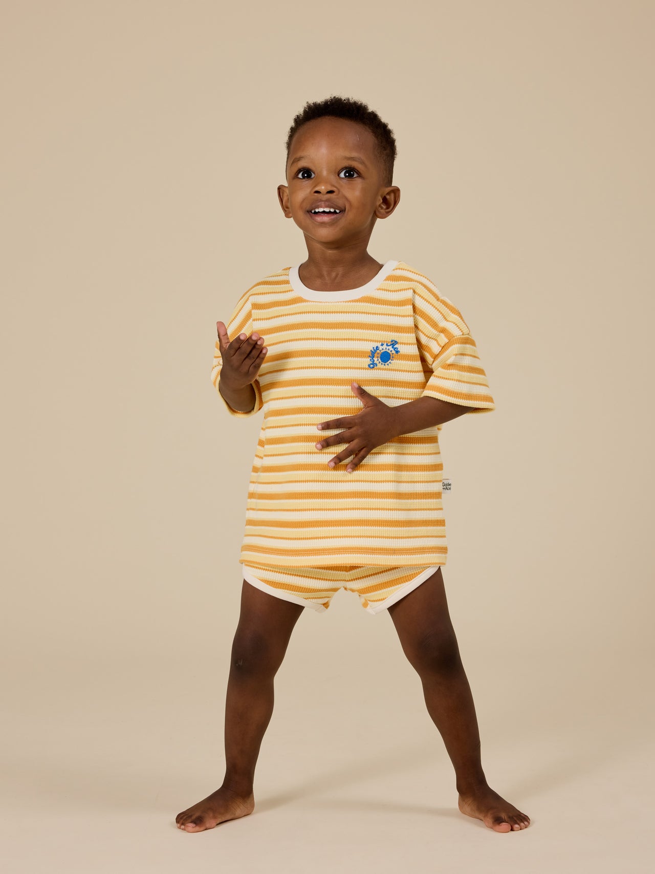 The Goldie + Ace Sunshine Stripe T-Shirt in Lemon/Golden pictured on a transparent background. The material is 100% cotton. It is a top made for babies, toddlers and kids.
