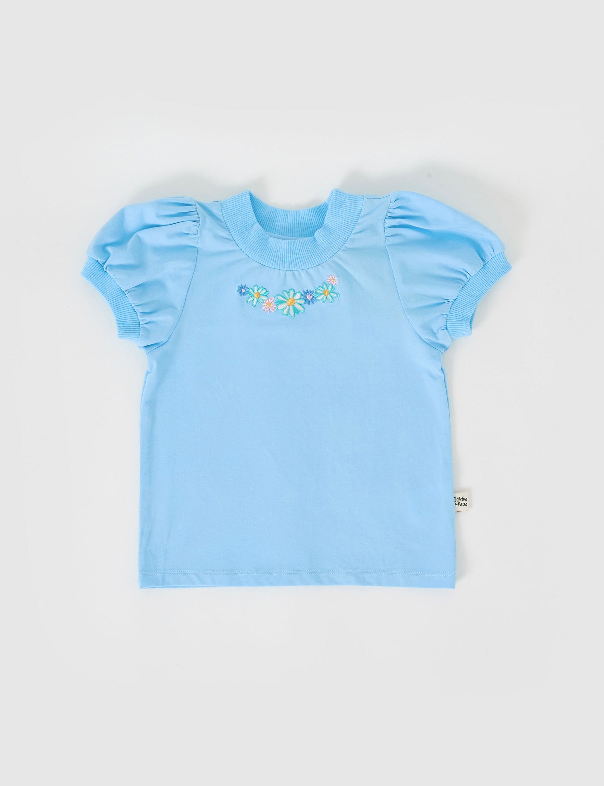 The Goldie + Ace Eden Embroidered Puff Sleeve T-Shirt in Sky Blue pictured on a grey background. The material is cotton jersey. It is a top made for babies, toddlers and kids.