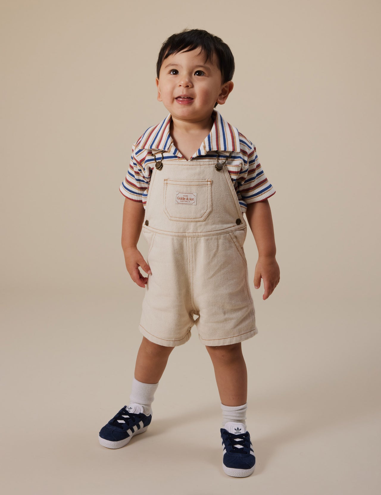 The Goldie + Ace Outback Stripe Rib Polo Shirt in Outback Stripe pictured on a grey background. The material is ribbed cotton. It is a top made for babies, toddlers and kids.