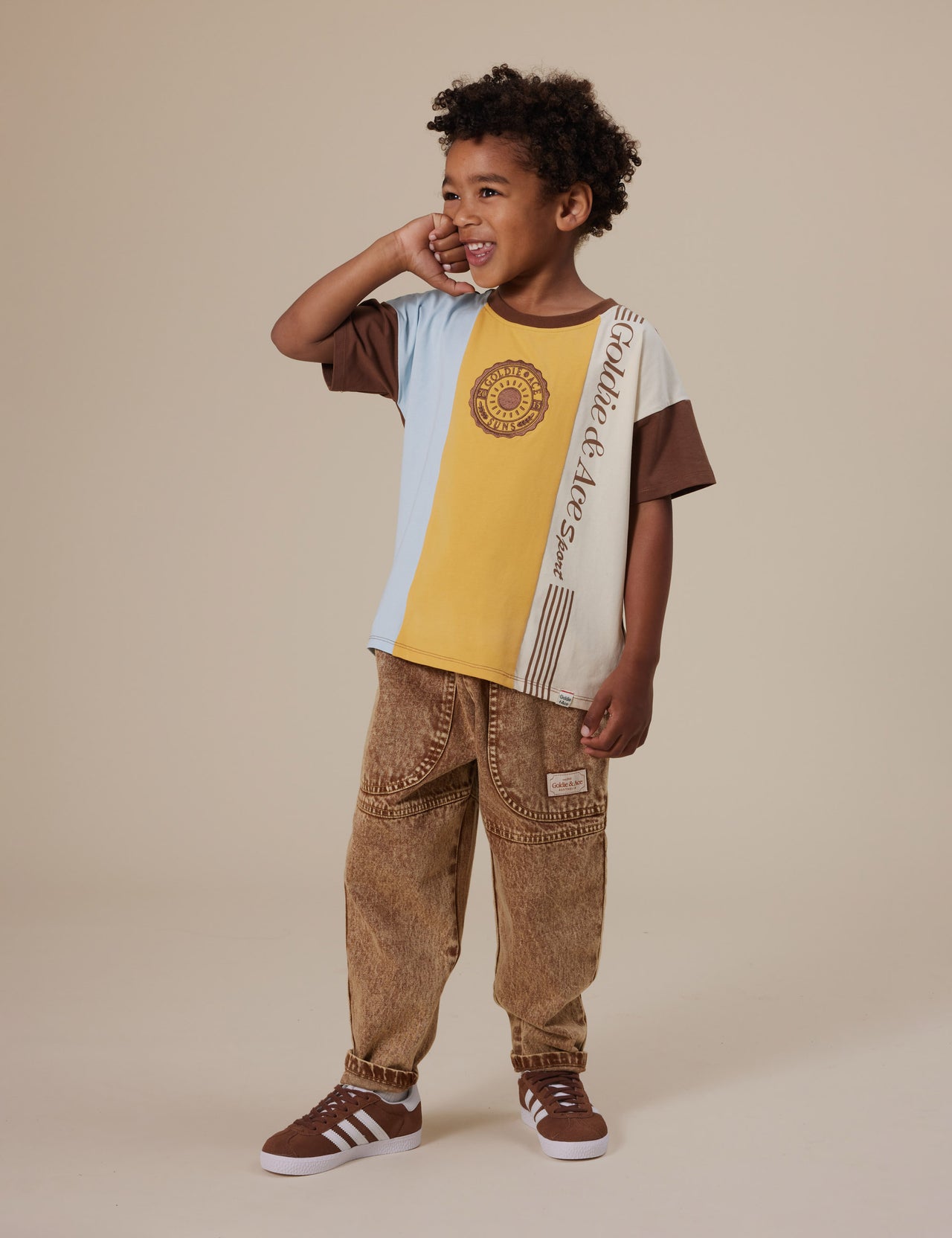 The Goldie + Ace Goldie Sports Day T-Shirt in Brown Golden Cream Blue pictured on a grey background. The material is cotton jersey. It is a top made for babies, toddlers and kids.