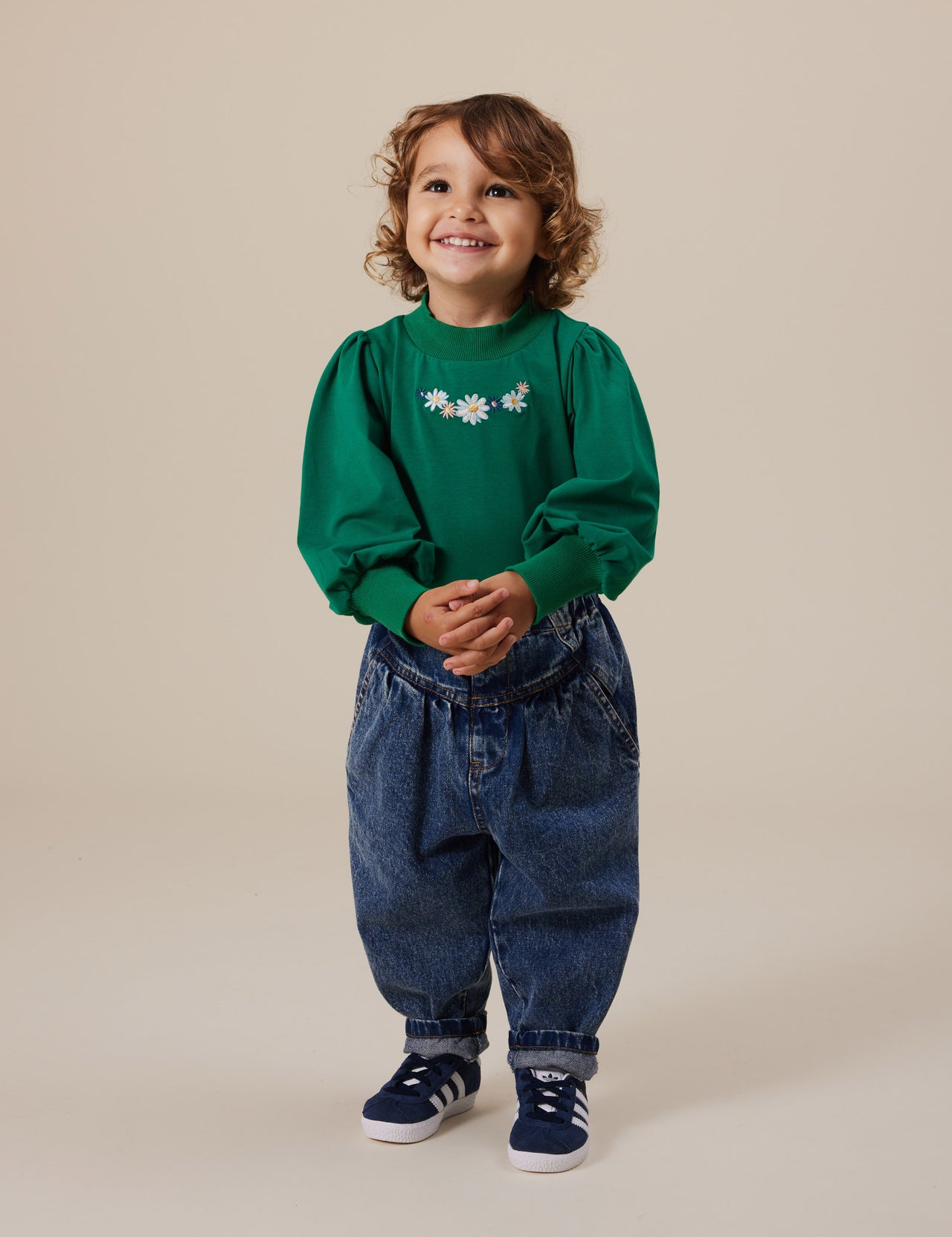 The Goldie + Ace Eden Embroidered Puff Sleeve Top in Bottle Green pictured on a grey background. The material is cotton jersey. It is a top made for babies, toddlers and kids.