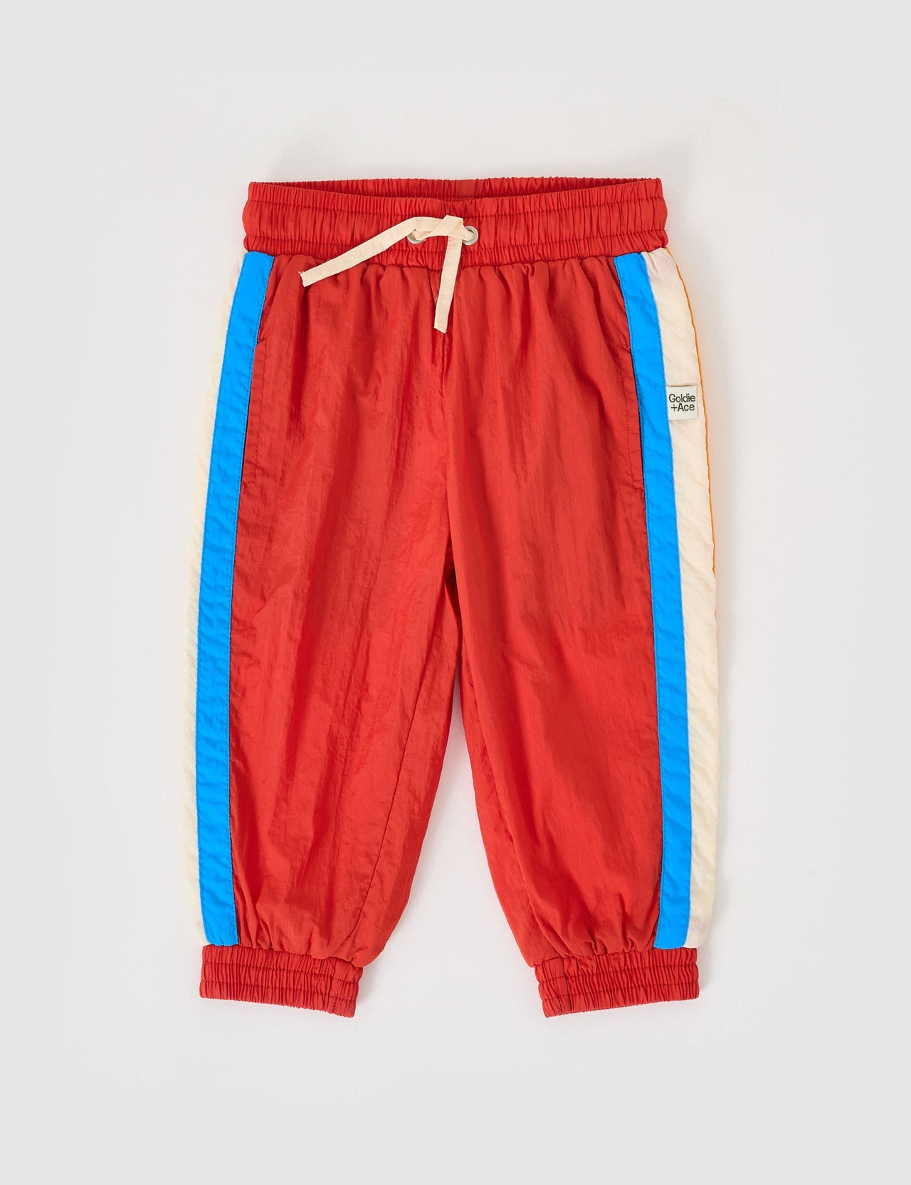 The Goldie + Ace Retro Lightweight Sporty Pants in Red pictured on a grey background. The material is poly & cotton with cotton lining. It is a bottom made for babies, toddlers and kids.