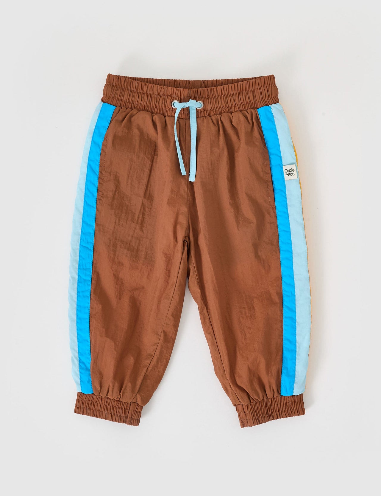 The Goldie + Ace Retro Lightweight Sporty Pants in Brown pictured on a grey background. The material is poly & cotton with cotton lining. It is a bottom made for babies, toddlers and kids.