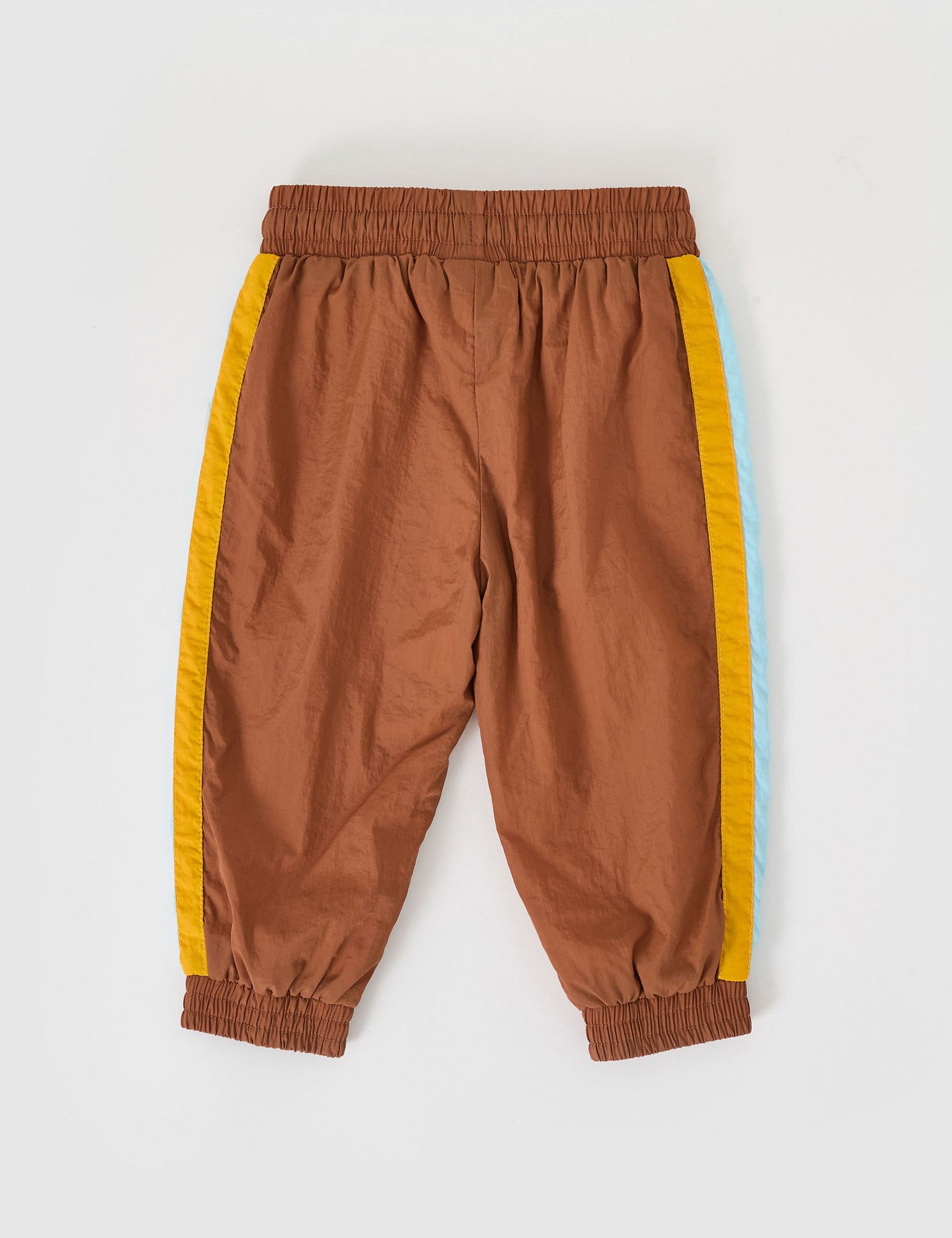 The Goldie + Ace Retro Lightweight Sporty Pants in Brown pictured on a grey background. The material is poly & cotton with cotton lining. It is a bottom made for babies, toddlers and kids.