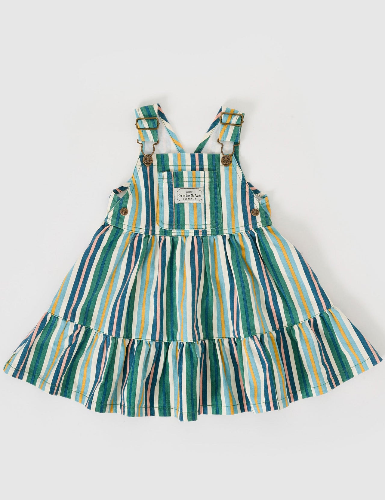 The Goldie + Ace Tully Tiered Pinafore Dress in Evergreen Stripe pictured on a grey background. The material is cotton twill. It is a dress made for babies, toddlers and kids.