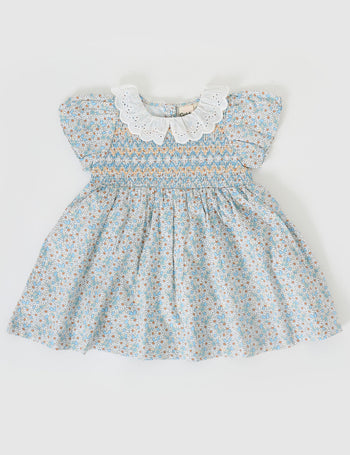 The Goldie + Ace Sunny Floral Flo Smocked Dress in Sunny Floral pictured on a grey background. The material is cotton. It is a dress made for babies, toddlers and kids.