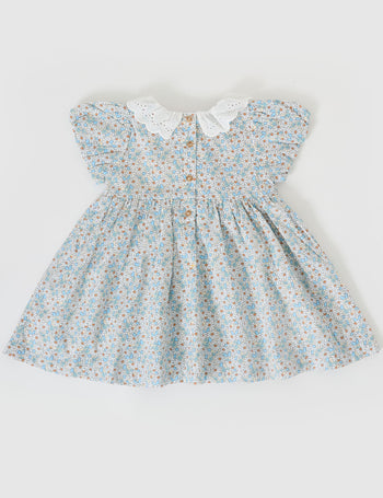 The Goldie + Ace Sunny Floral Flo Smocked Dress in Sunny Floral pictured on a grey background. The material is cotton. It is a dress made for babies, toddlers and kids.