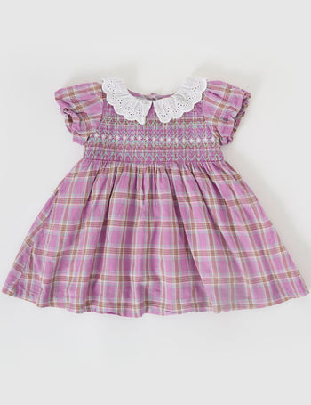 The Goldie + Ace Mauve Check Flo Smocked Dress in Mauve Check pictured on a grey background. The material is cotton. It is a dress made for babies, toddlers and kids.