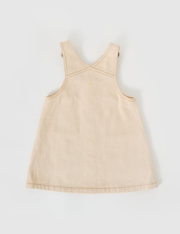 The Goldie + Ace Penelope Pinafore Pocket Dress in Oat pictured on a grey background. The material is cotton twill. It is a dress made for babies, toddlers and kids.