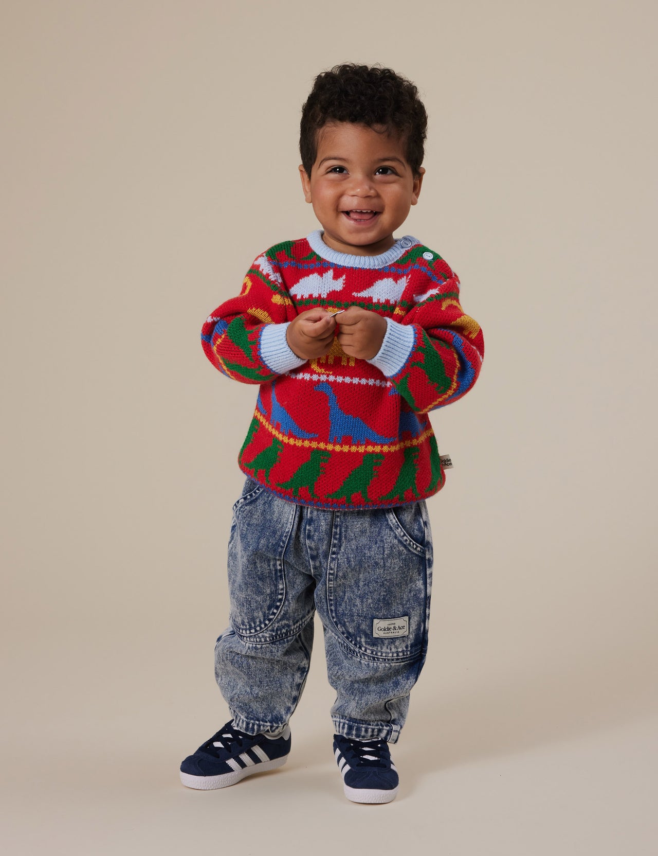 The Goldie + Ace Dino Knit Jumper in Burgundy pictured on a grey background. The material is super soft wool blend. It is a knit made for babies, toddlers and kids.