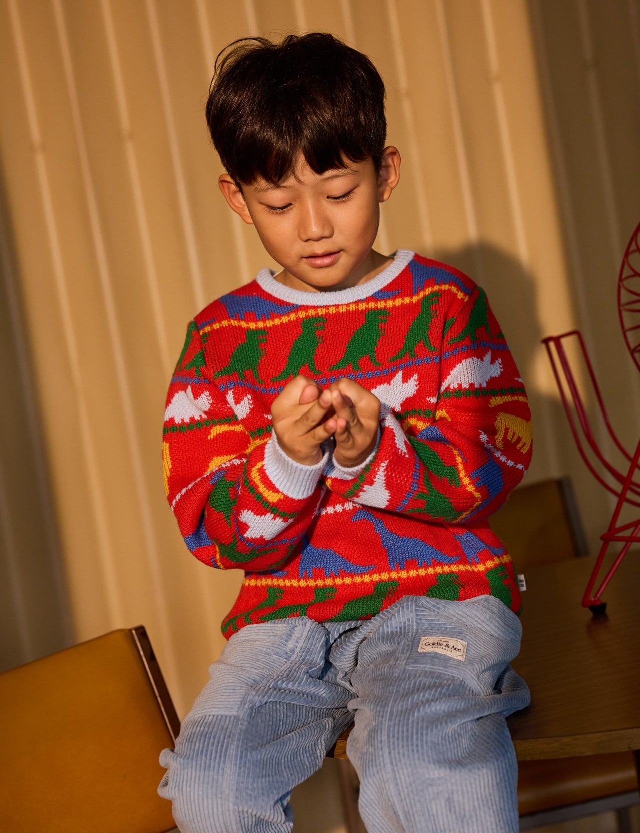 The Goldie + Ace Dino Knit Jumper in Burgundy pictured on a grey background. The material is super soft wool blend. It is a knit made for babies, toddlers and kids.