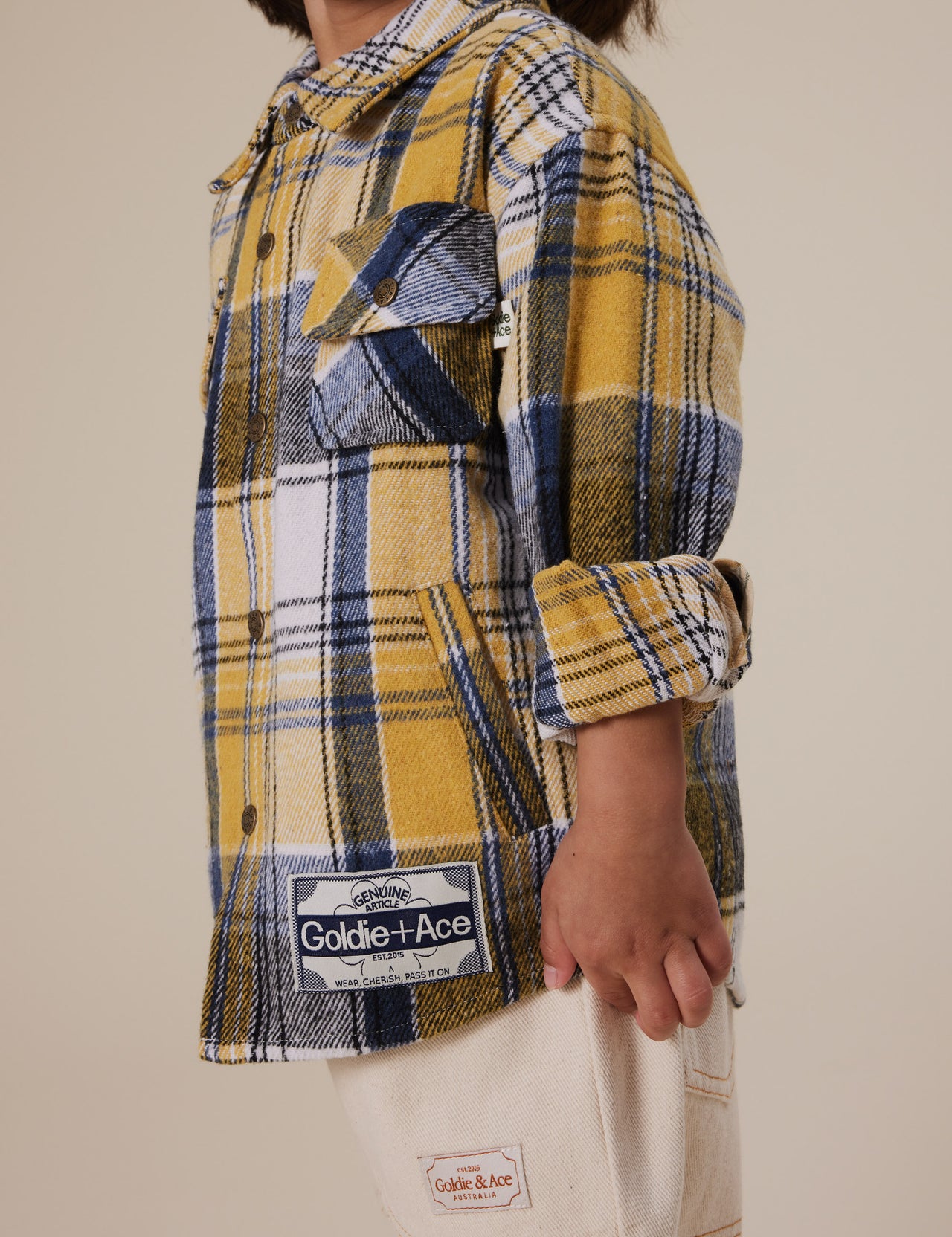 The Goldie + Ace Rowan Check Shirt in Golden pictured on a grey background. The material is poly & cotton with cotton lining. It is a top made for babies, toddlers and kids.