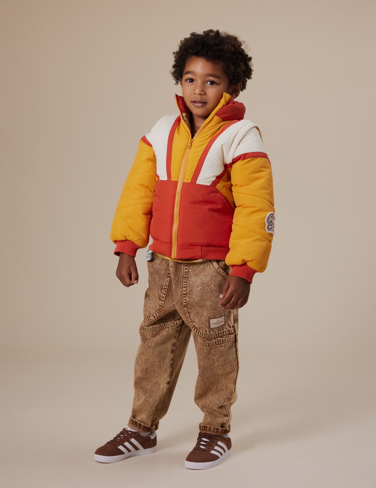 The Goldie + Ace Andy Vest/Jacket in Golden Red pictured on a grey background. The material is poly with poly fill. It is a jacket made for babies, toddlers and kids.